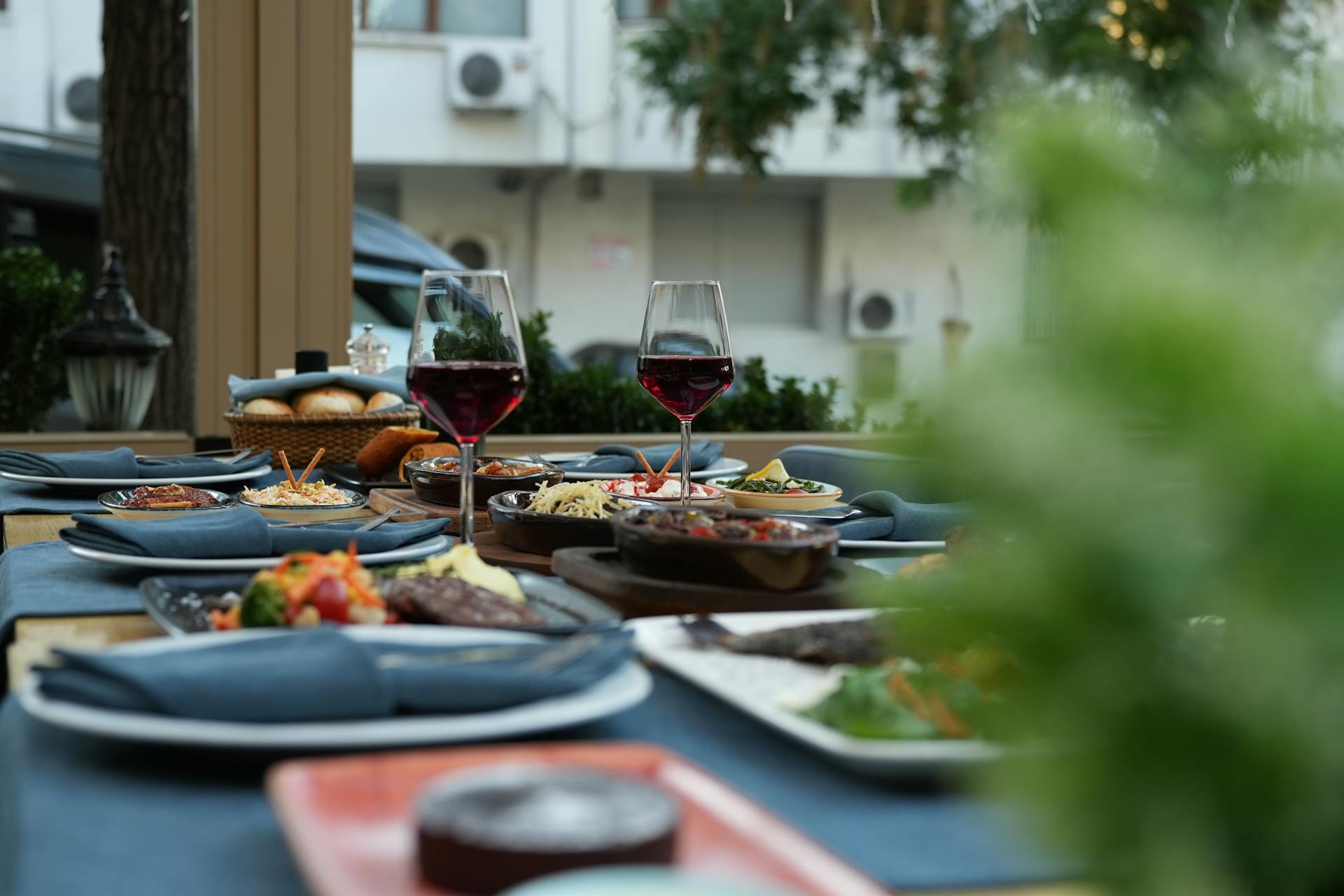 A restaurant table set with food and glasses of red wine