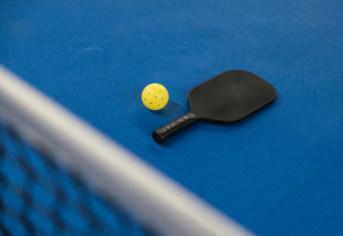 A pickleball paddle and ball on a blue court